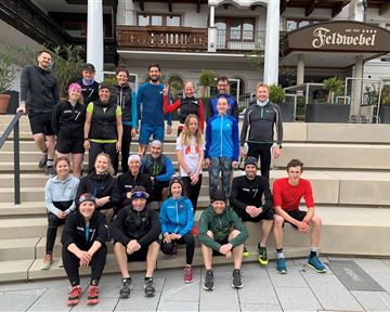 Eine Gruppe von Menschen steht auf Treppenstufen vor einem Hotel. Alle sind sportlich gekleidet und posieren freundlich für das Foto.