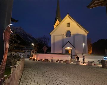 Eine charmante Kirche bei Nacht mit einem spitzen Turm. Der Außenbereich ist mit Lichtern geschmückt, die eine festliche Atmosphäre schaffen.