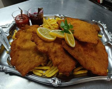 Ein großer Teller mit knusprigem Schnitzel, serviert mit Pommes frites und zwei verschiedenen Dips. Frische Zitronenscheiben und ein Minzblatt verleihen dem Gericht eine dekorative Note.