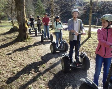 Eine Gruppe von Menschen fährt auf Segways in der Natur. Die Sonne scheint, und es gibt Bäume im Hintergrund.