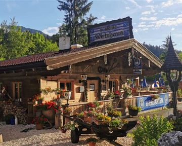 Ein charmantes Holzgebäude mit einem traditionellen bayerischen Stil. Der Garten ist mit bunten Blumen und Pflanzen geschmückt.
