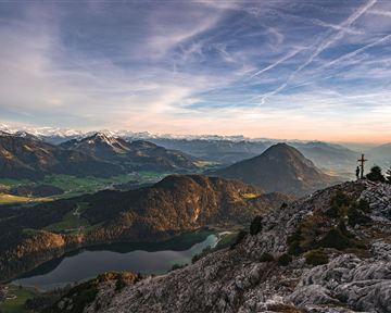 An impressive mountain landscape with snow-capped peaks and a clear lake in the valley. The sky is infused with gentle colors and clouds.