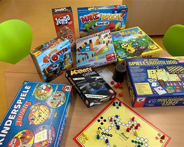 A selection of board games is spread out on a table. The games are colorful and range from classic to modern children's games.