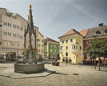 A beautiful square with a fountain in the center and colorful buildings in the background. The atmosphere is calm and inviting.