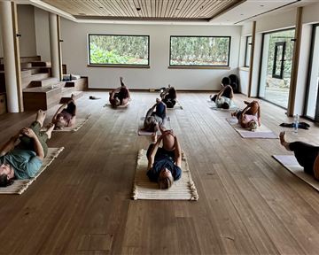 Ein ruhiger Yogaraum mit mehreren Personen, die auf Matten liegen. Die sanfte Beleuchtung schafft eine entspannende Atmosphäre.