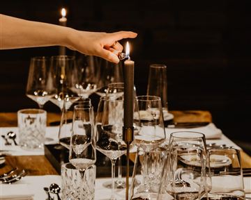 An elegantly set table with glasses and cutlery. A hand lighting a candle that creates a cozy atmosphere.