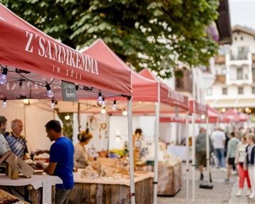 Ein lebendiger Marktplatz bei Dämmerung mit Ständen, die lokale Produkte anbieten. Menschen schlendern durch die Gassen und genießen die Atmosphäre.