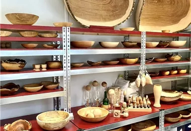 A shelf with various handcrafted wooden bowls and objects. The exhibits showcase the natural grain of the wood and vary in shape and size.