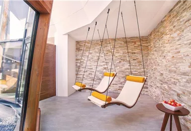 A modern room with two hanging loungers and an attractive stone wall. Next to the chairs is a small table with apples.