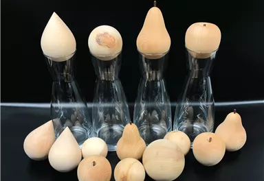 Three glass carafes with wooden molds in various fruit and vegetable shapes. The wooden objects are arranged in different sizes and shapes.