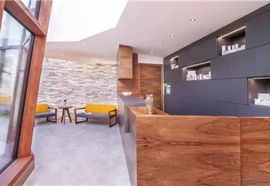 A modern reception area with wooden furniture and a bright, inviting ambiance. The walls are decorated with elegant stone cladding.
