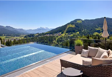 Ein luxuriöser Infinity-Pool mit Blick auf die Berge und die umliegende Natur. Gemütliche Sitzecke und Sonnenschirm sorgen für Entspannung und Komfort.