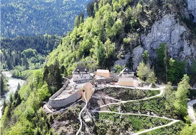 Eine malerische Landschaft mit einem kleinen Gebäude auf einem Hügel. Umgeben von grünen Wäldern und Bergen.