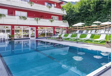 A beautiful pool with loungers and umbrellas outdoors. In the background, a modern building with balconies is visible.