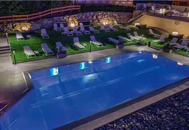 A modern pool with clear blue water and comfortable loungers. The garden area is well-lit and has an inviting atmosphere.