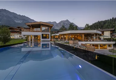 Ein modernes Gebäude mit großen Fenstern und einem schönen Infinity-Pool. Im Hintergrund sind majestätische Berge und Bäume zu sehen.