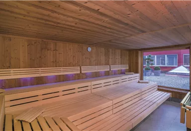 A modern sauna with wooden surfaces and comfortable loungers. Through the large windows, one looks out onto a cozy outdoor area.