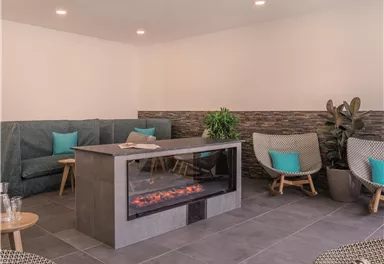A modern, cozy living room with comfortable armchairs and an elegant fireplace. The walls are light, and there are plants that create a relaxing atmosphere.
