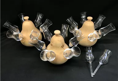 Three decorative wooden objects with glasses attached to the sides. They have a unique, creative shape and are placed against a dark background.
