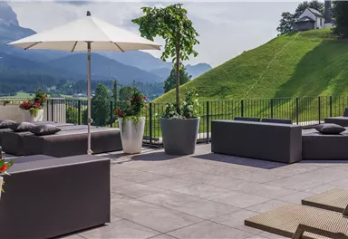 A modern terrace with comfortable seating and sun umbrellas. In the background, a green landscape stretches out with gentle hills.