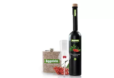 A bottle of liqueur with red berries, a glass, and a decorative box. The product is from the brand Aggstein.