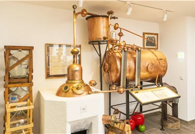An old distillation facility with copper components and various containers. In the background, some informational posters can be seen.