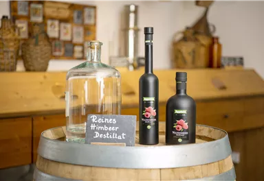 A wooden tabletop with a large glass bottle and two bottles of raspberry distillate. Next to it is a sign that reads "Pure Raspberry Distillate."