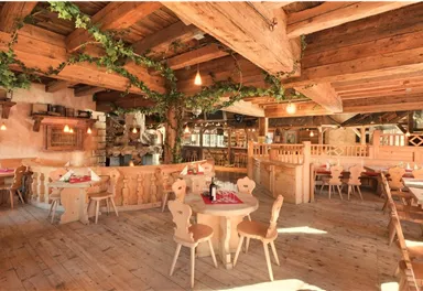 A cozy restaurant with wooden interiors and warm lighting. The tables are beautifully set, and there are green plants on the walls.