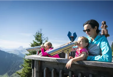 A mother and her two daughters are looking at the mountains with telescopes. The clear sky and the view create a relaxing atmosphere.