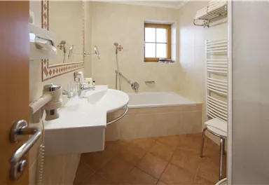A modern bathroom with a bathtub and shower. The walls are light, and a window lets in daylight.