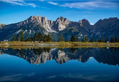 Eine beeindruckende Berglandschaft mit klaren Gipfeln, die sich im ruhigen Wasser spiegelt. Der Himmel ist blau und wolkenlos.