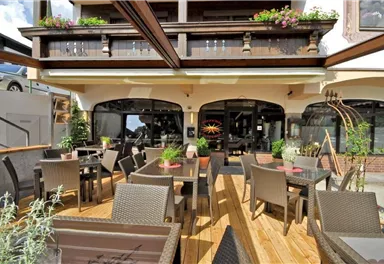 Eine einladende Terrasse mit eleganten Möbeln. Üppige Pflanzen schmücken den Bereich vor einem gemütlichen Restaurant.