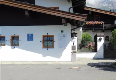 A traditional alpine house with a parking sign. The facade is painted in white and has small windows with wooden frames.
