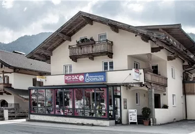 A traditional building in the Alps with a commercial area on the ground floor. The weather is cloudy, beautiful mountain scenery in the background.