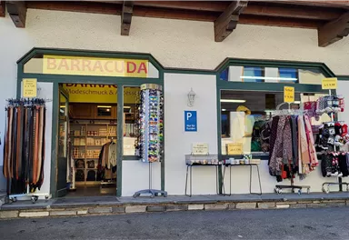 Ein Geschäft mit dem Namen "Barracuda" ist zu sehen. Davor hängen verschiedene Gürtel und Bekleidungsartikel.