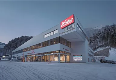 Ein modernes Gebäude mit einem großen Schild für SkiWelt Ellmau. Es liegt in einer winterlichen Landschaft mit Schnee und Bergen im Hintergrund.