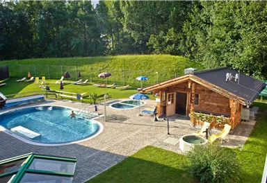 Ein schöner Außenbereich mit einem Pool und Whirlpools. Im Hintergrund gibt es eine grüne Wiese und eine Holz-Hütte.