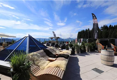 A cozy terrace with modern loungers and plants. In the background, mountains can be seen under a clear sky.