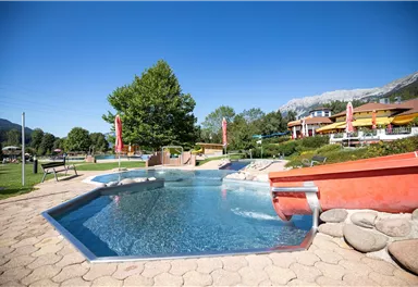 Ein schöner Poolbereich mit glattem Wasser und entspannenden Liegen. Umgeben von üppigem Grün und einem klaren blauen Himmel.