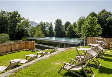 Ein schöner Außenbereich mit Liegen und einem modernen Pool. Umgeben von üppigem Grün und Bäumen.