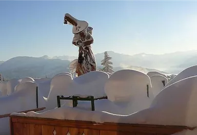 A snowy landscape with many snow-covered hills. In the foreground stands a statue surrounded by snow, while the sun is shining.