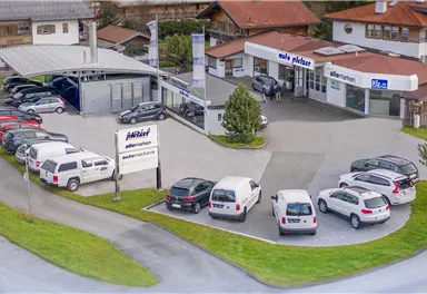 Ein Autohaus mit mehreren Fahrzeugen auf dem Gelände. Es gibt ein modernes Gebäude und eine große Auswahl an Autos.