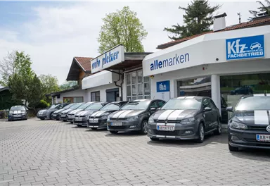 Eine Reihe von Autos mit gestreiftem Design steht vor einem Gebäude mit großen Schildern. Im Hintergrund sind Bäume und ein klarer Himmel sichtbar.
