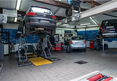 Eine Kfz-Werkstatt mit mehreren Autos auf Hebebühnen. Die Wände sind mit Werkzeugen und Ausrüstungen ausgestattet.