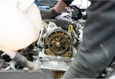 Ein Mechaniker arbeitet an einem Auto-Motor. Teile des Motors sind sichtbar, einschließlich eines Zahnradmechanismus.