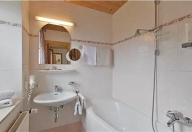 Ein modernes Badezimmer mit einer Badewanne, einem Waschbecken und einer Dusche. Helle Fliesen und Holzdetails sorgen für ein einladendes Ambiente.