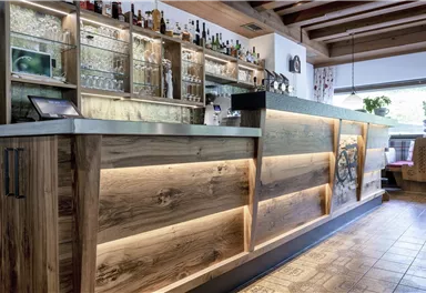 Eine moderne Bar mit einem Holztheke und beleuchteten Akzenten. Im Hintergrund sind Glasregale mit verschiedenen Getränken zu sehen.