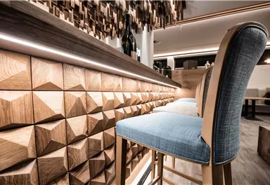An elegant bar area with decorative wood paneling. The chairs have a modern, comfortable upholstery in blue.