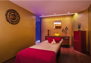 Ein stilvoller Spa-Raum mit einem Massagebett und warmen Gelbtönen. Dekorative Elemente und sanftes Licht sorgen für eine entspannende Atmosphäre.