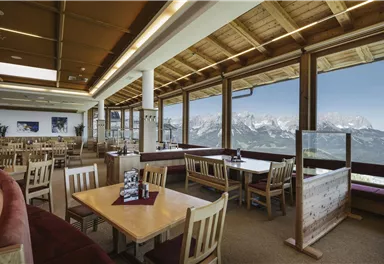 A cozy restaurant with large windows and a view of the mountains. The tables are neatly set and there is a pleasant, inviting atmosphere.